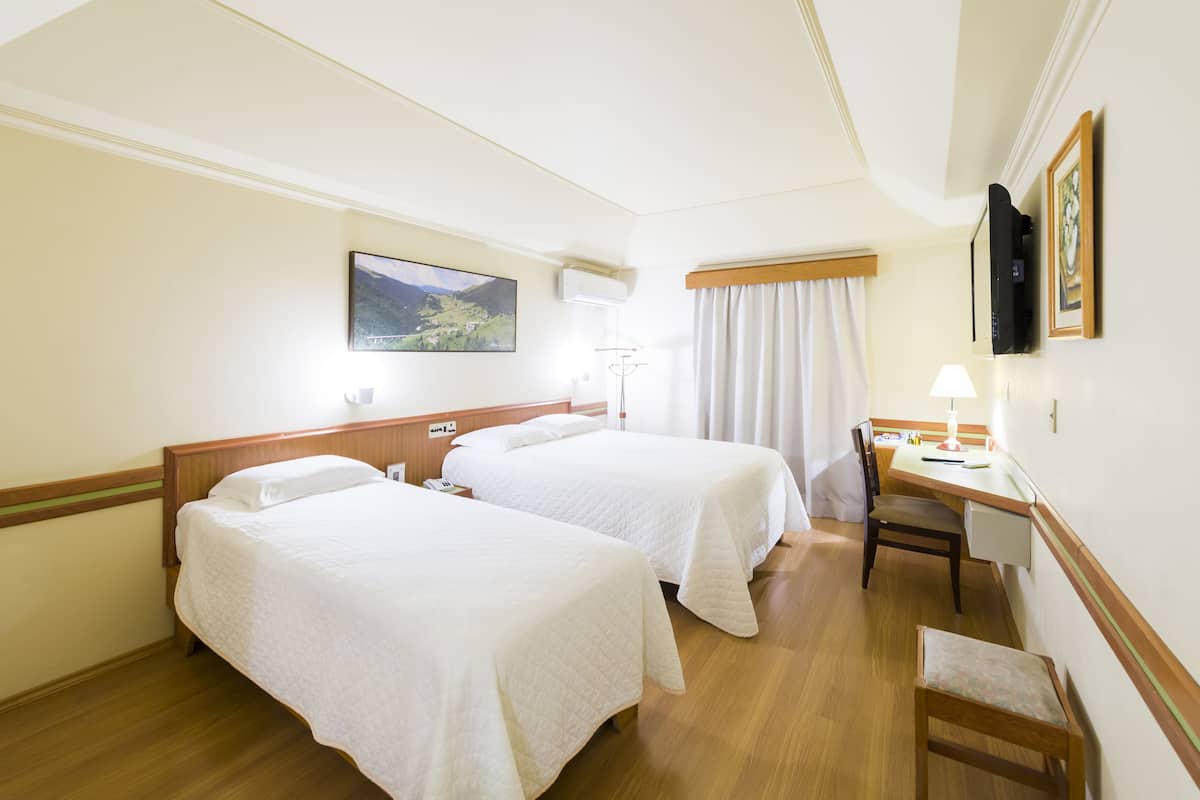 A hotel room with two beds, a desk, a chair, a lamp, and a painting on the wall.
