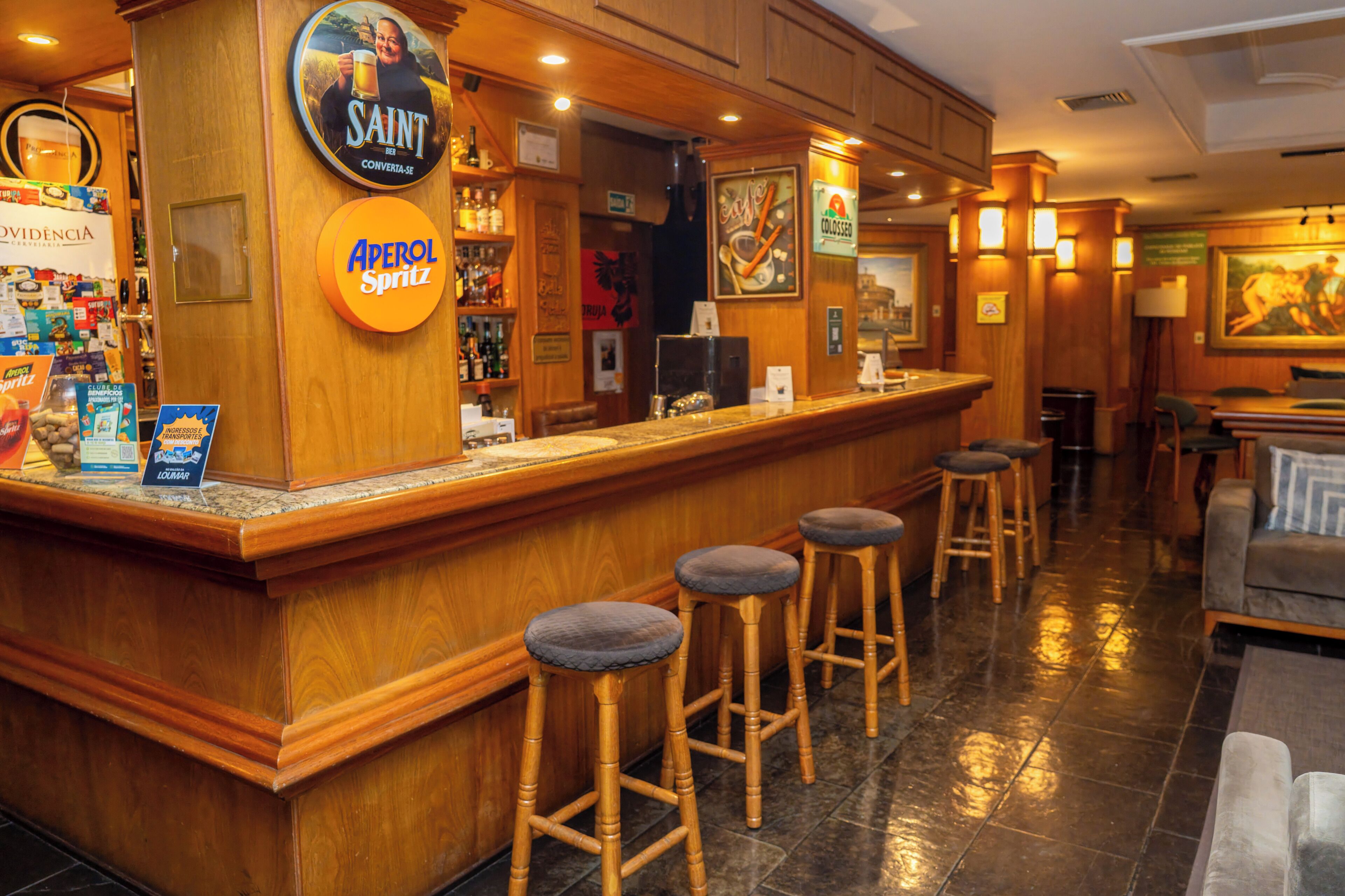 Un espace bar avec un comptoir en bois, des tabourets et divers panneaux, notamment les mots « SAINT » et « Aperol Spritz ».