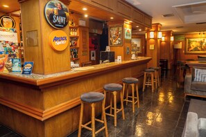 Zona de bar amb un mostrador de fusta, tamborets i diferents senyals que inclouen 'SAINT' i 'Aperol Spritz'.