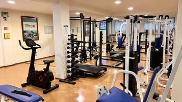 Un gimnasio con varios equipos de ejercicio, incluyendo cintas de correr, máquinas de pesas y pesas sueltas.