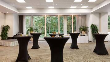 A conference room with four black tables, large windows with a view of trees, and a carpeted floor.