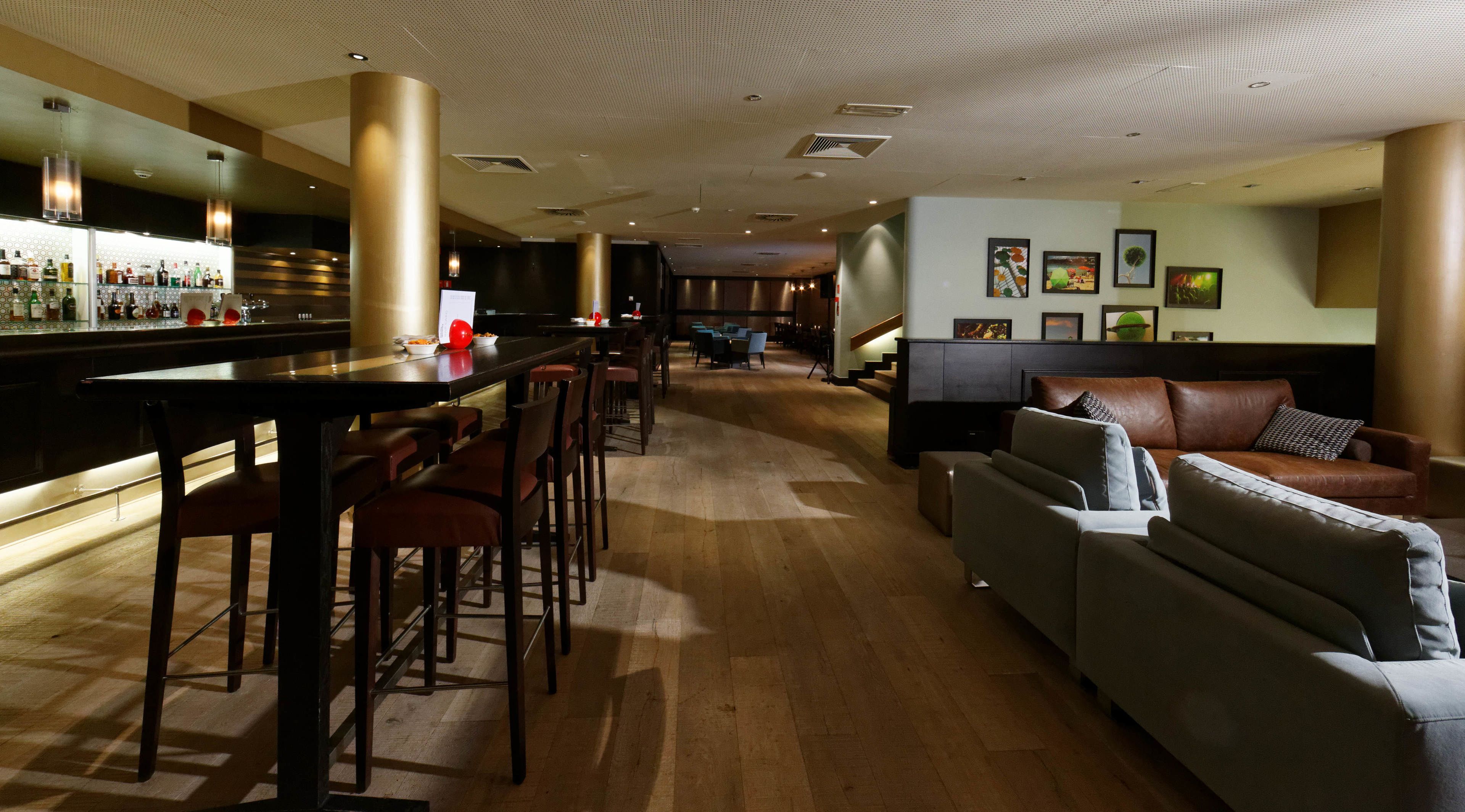 A bar area with stools and a bar counter, a seating area with a sofa and chairs, and a wall with framed pictures.
