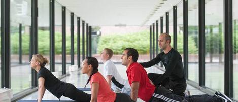 Un grupo de personas realizando ejercicios de yoga en un espacio interior moderno con ventanas amplias y un pasillo de vidrio.