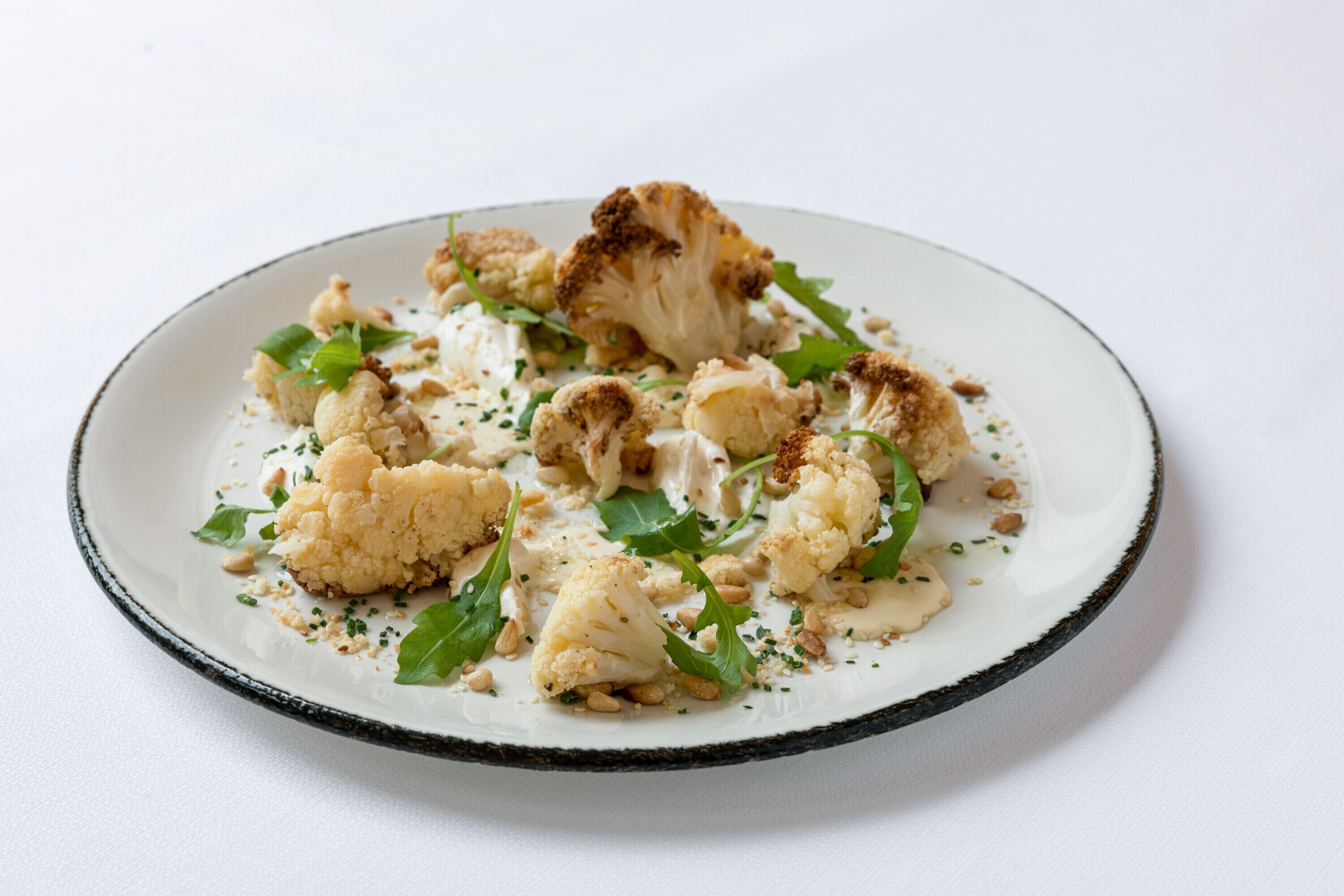 Un plato de coliflor con salsa cremosa y adornos.