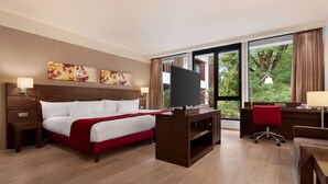 Une chambre d’hôtel avec un lit, un bureau, une télévision et de grandes fenêtres.