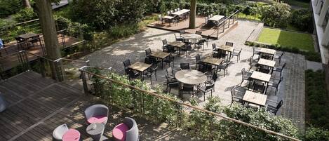 An outdoor patio area with multiple tables and chairs, surrounded by greenery and trees.