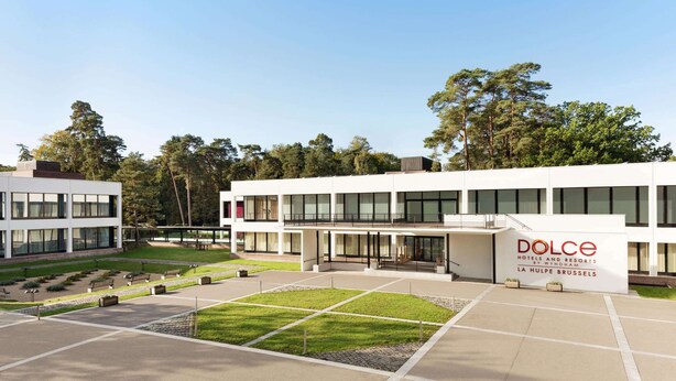Un hôtel moderne doté d’un vaste espace extérieur, d’une enseigne indiquant « Dolce Hotels and Resorts » et offrant une vue sur un ciel dégagé.