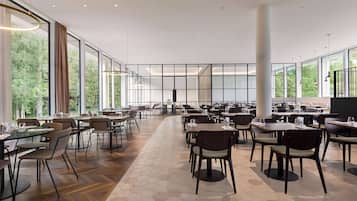 Un amplio comedor interior con múltiples mesas y sillas, grandes ventanales que ofrecen vistas a zonas verdes, y un diseño arquitectónico moderno con suelo de baldosas hexagonales.