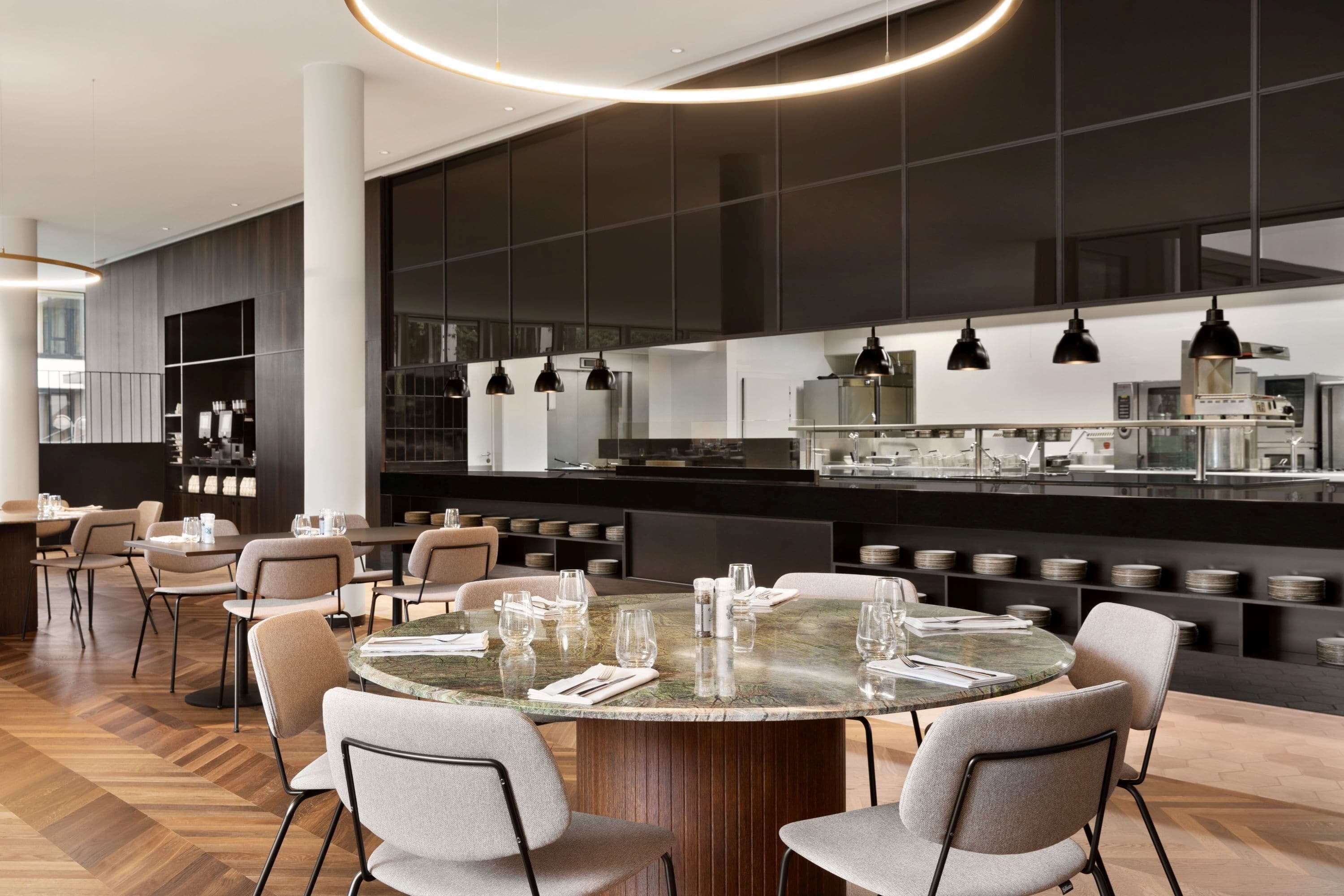 Un restaurante moderno con mesas redondas, sillas y una amplia zona de cocina.