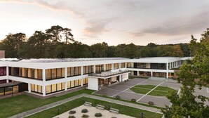 Un bâtiment moderne doté d’une cour intérieure, avec un espace central ouvert agrémenté de bancs et de jardinières, le tout entouré d’une façade blanche et de grandes fenêtres.