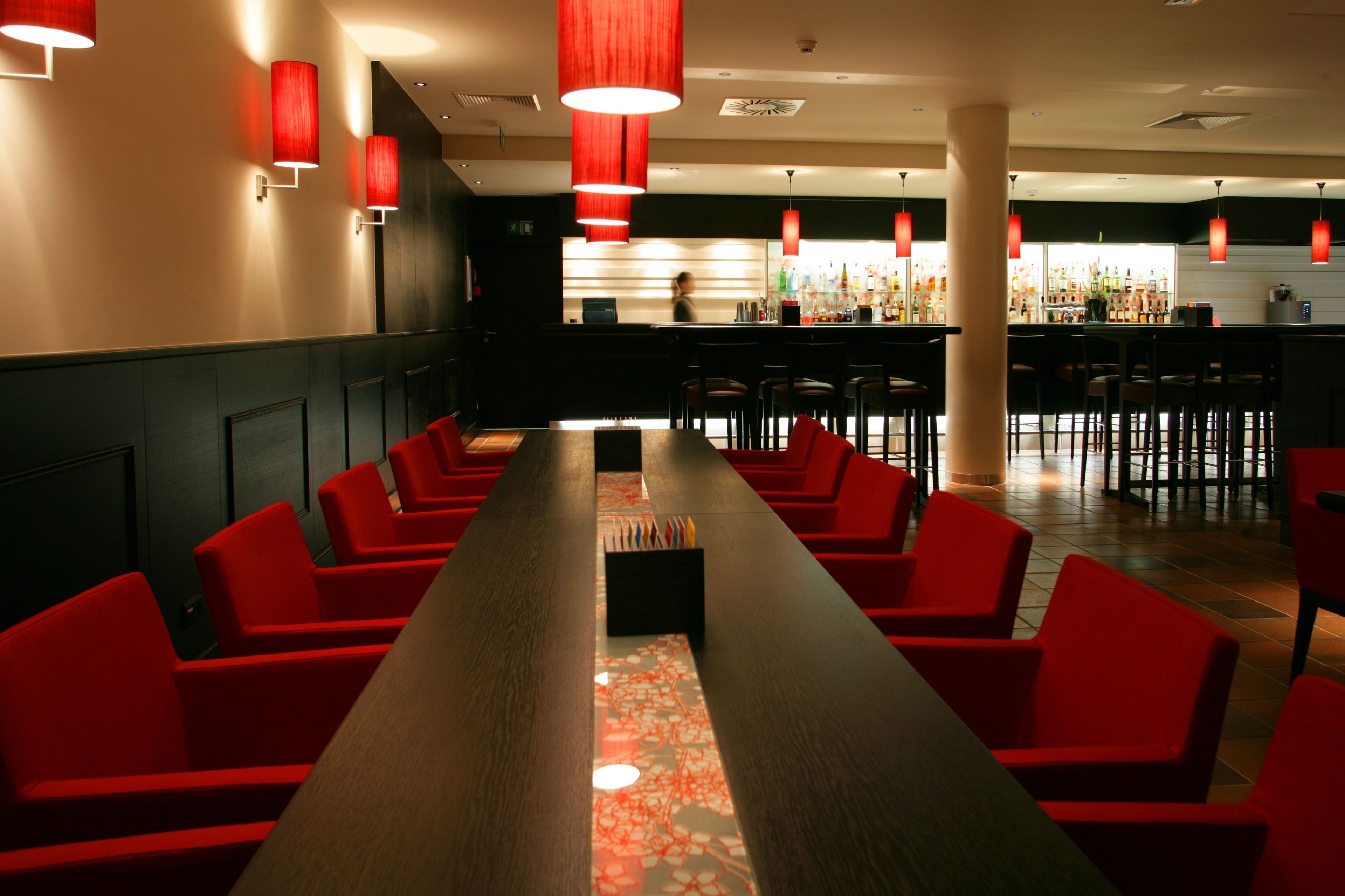 Een restaurant met rode stoelen, een lange tafel en rode hanglampen.