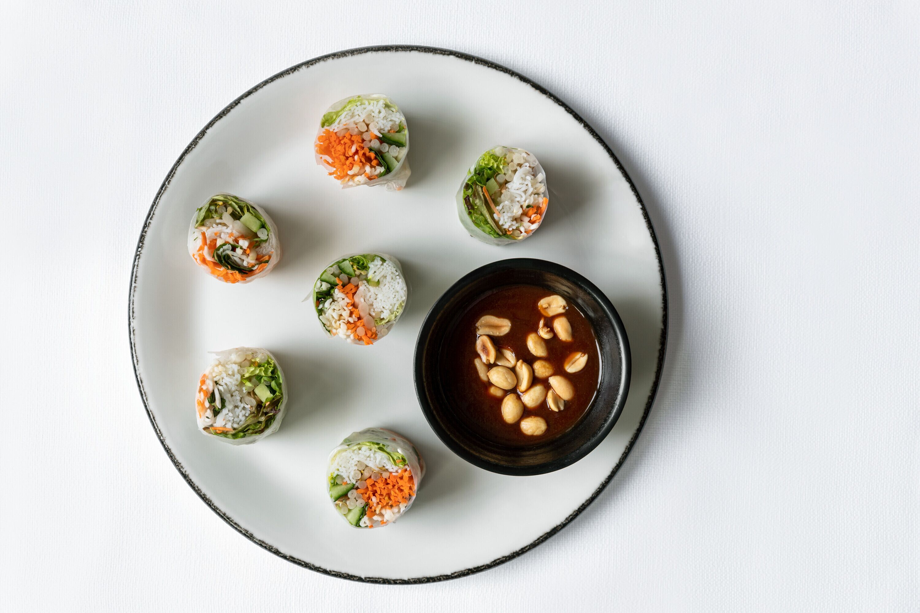 Un plato con seis rollitos de primavera y un tazón de salsa para mojar.