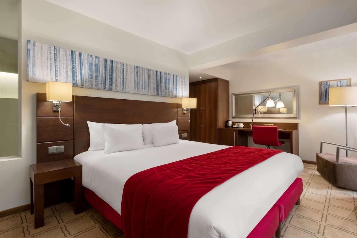 Une chambre d’hôtel avec un grand lit, un bureau, une chaise, une armoire et un miroir.