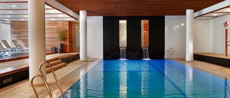 Une piscine dotée d’un plafond en bois, de colonnes blanches et d’une cascade décorative.