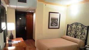 A hotel room with a bed, a desk with a lamp, a framed picture on the wall, and a door leading to another room. - Hotel La Finca del Minero (Zacatecas)