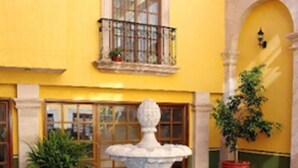 A courtyard with a central fountain, potted plants, and a yellow building with a window and balcony. - Hotel La Finca del Minero (Zacatecas)