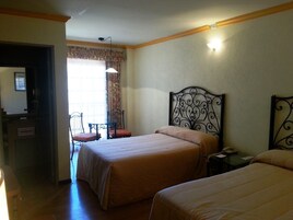 Una habitación de hotel con dos camas, un escritorio con teléfono y una silla cerca de una ventana con cortinas.