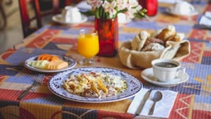 A breakfast table with plates of food, a glass of orange juice, a cup of coffee, and a vase of flowers. - Hotel La Finca del Minero (Zacatecas)