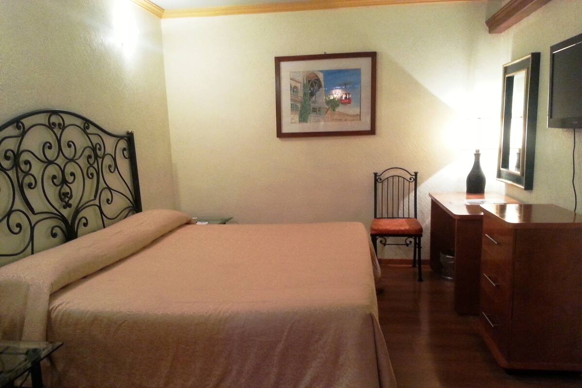 Een slaapkamer met een bed, een stoel, een dressoir en een ingelijst schilderij aan de muur.