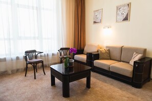 Uma sala de estar com sofá, duas poltronas, uma mesa de centro e um vaso com flores.