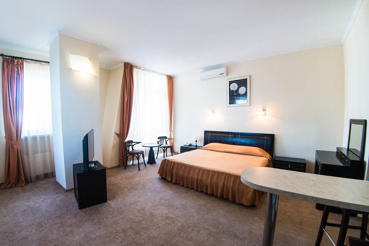 A hotel room with a bed, a desk, a chair, a TV, and a table.