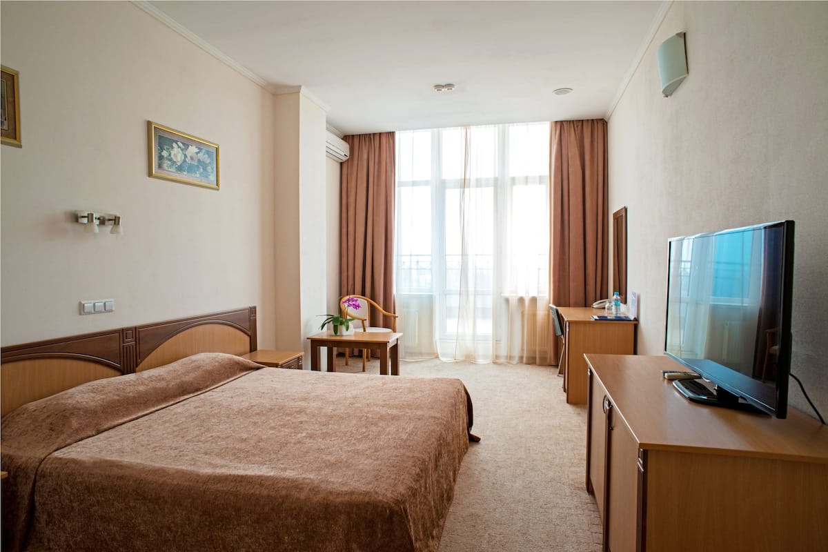 A hotel room with a bed, a desk, a television, and a window with curtains.
