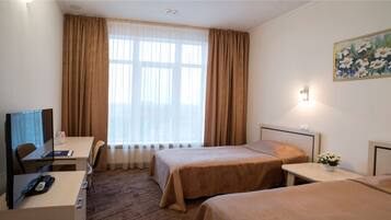 A hotel room with two beds, a desk, a chair, a television, and a painting on the wall.