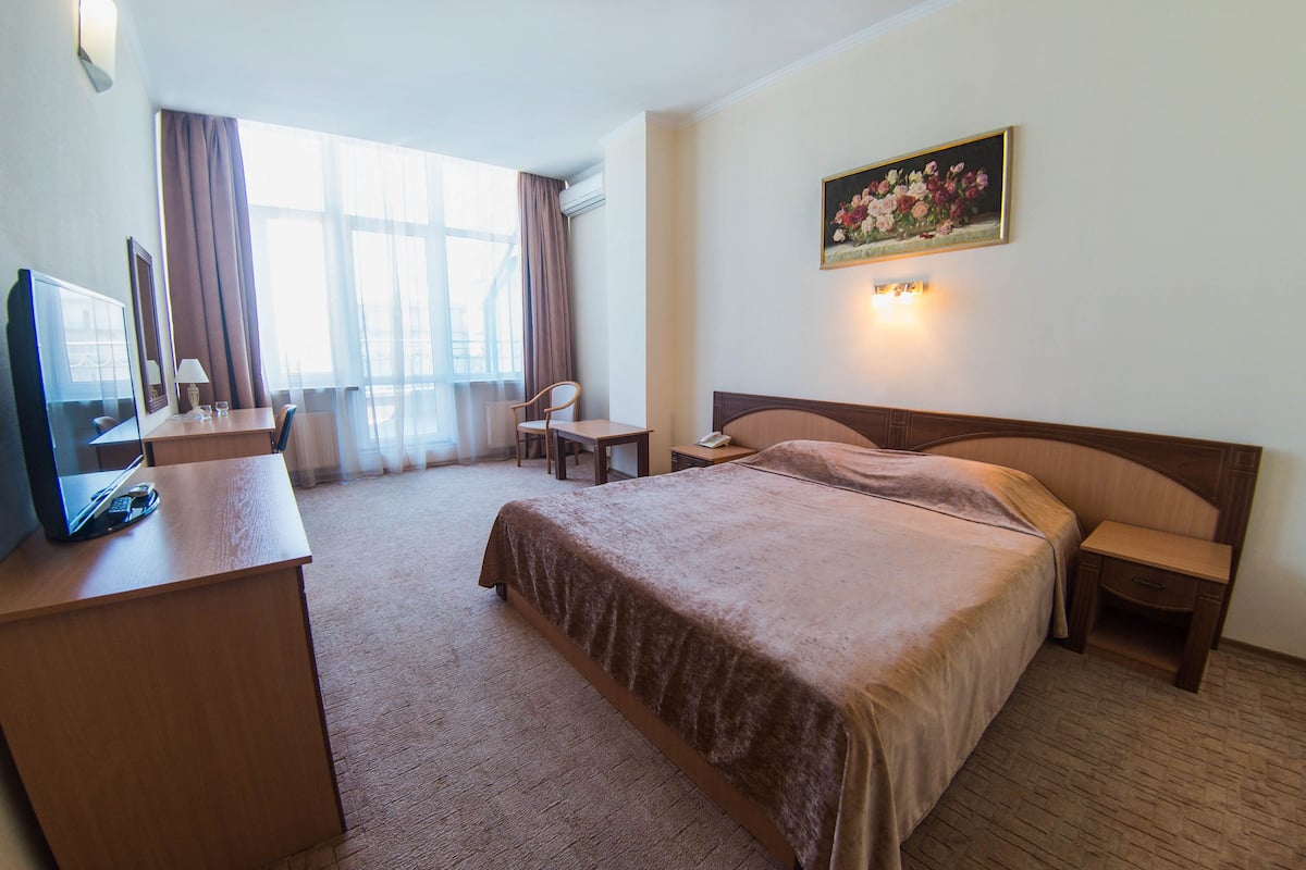 A hotel room with a large bed, a desk with a computer, a chair, and a painting on the wall.