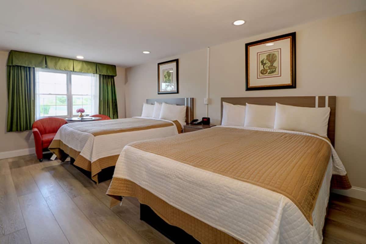 A hotel room with two beds, a red chair, and a window with green curtains.