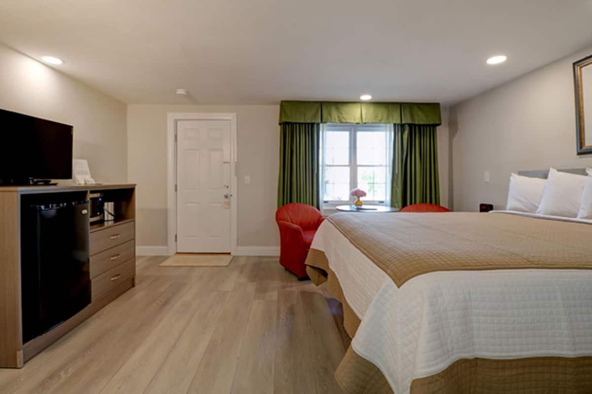 A hotel room with a bed, a TV, a desk with a computer, a chair, and a window with curtains.