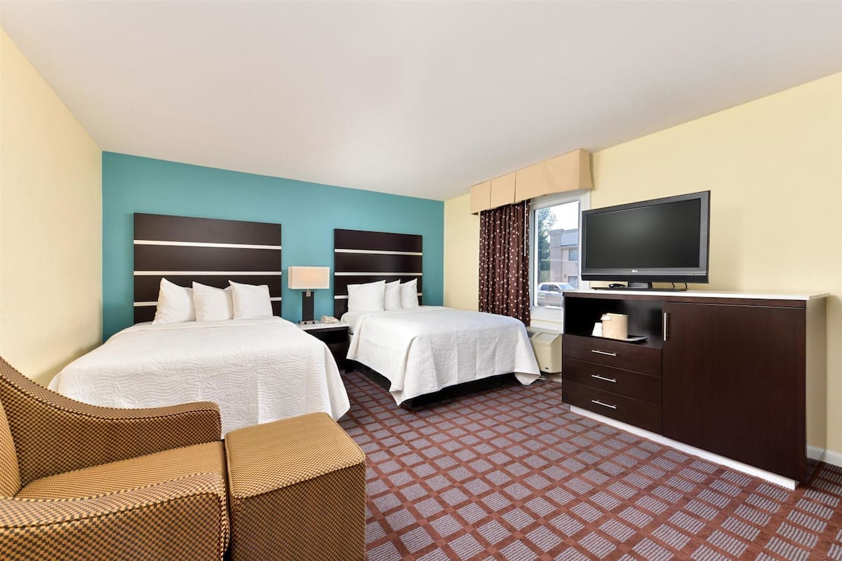 A hotel room with two beds, a TV, a desk, and a chair.