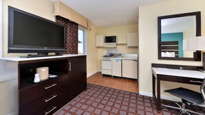 Habitación de hotel compacta con televisión de pantalla plana, kitchenette, escritorio con silla y un espejo grande.