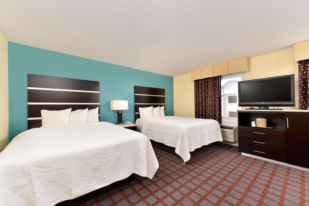A hotel room with two beds, a TV, a desk, and a window with curtains.