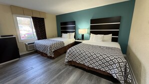 Habitación de hotel con dos camas, un escritorio, una lámpara y una ventana con cortinas.