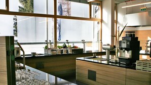 A modern kitchen with a central island, stainless steel appliances, and a view of the outdoors through large windows. - Cube Savognin (Surses)