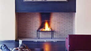 A fireplace with a fire, a TV mounted above it, and a person lying on a couch facing the fireplace. - Cube Savognin (Surses)