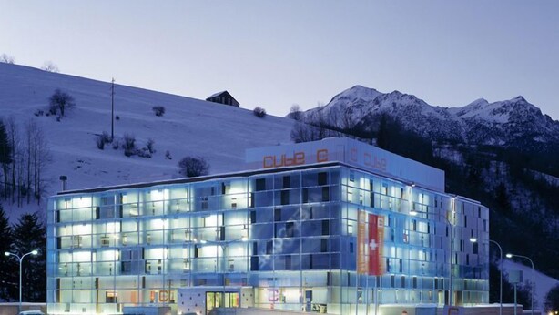 A modern building with a glass facade, surrounded by snow-covered mountains. - Cube Savognin (Surses)