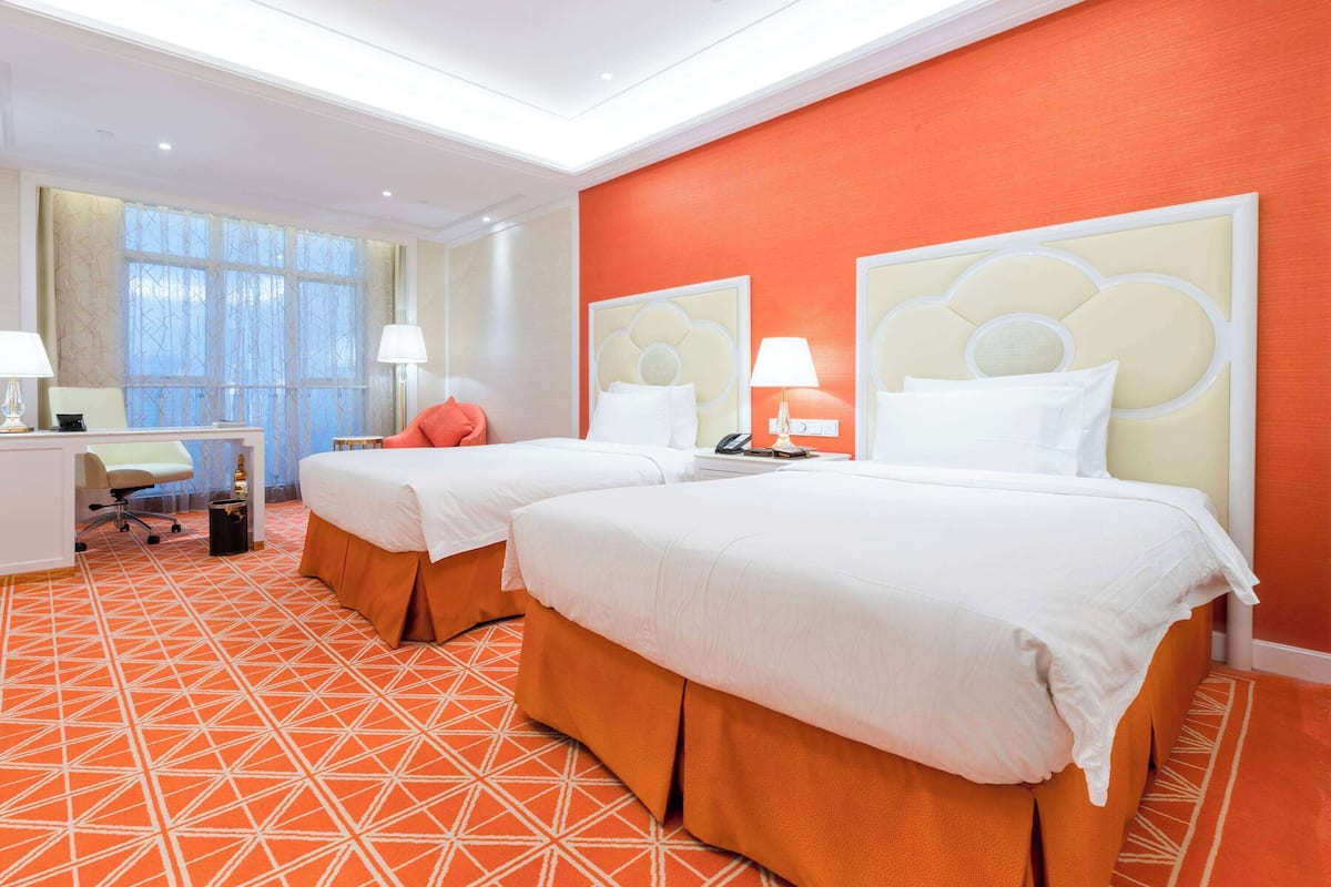 A hotel room with two beds, a desk, and a chair.