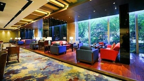 Eine großzügige Lobby mit einem großen Teppich, mehreren Sitzbereichen und großen Fenstern mit Blick auf Grünflächen.