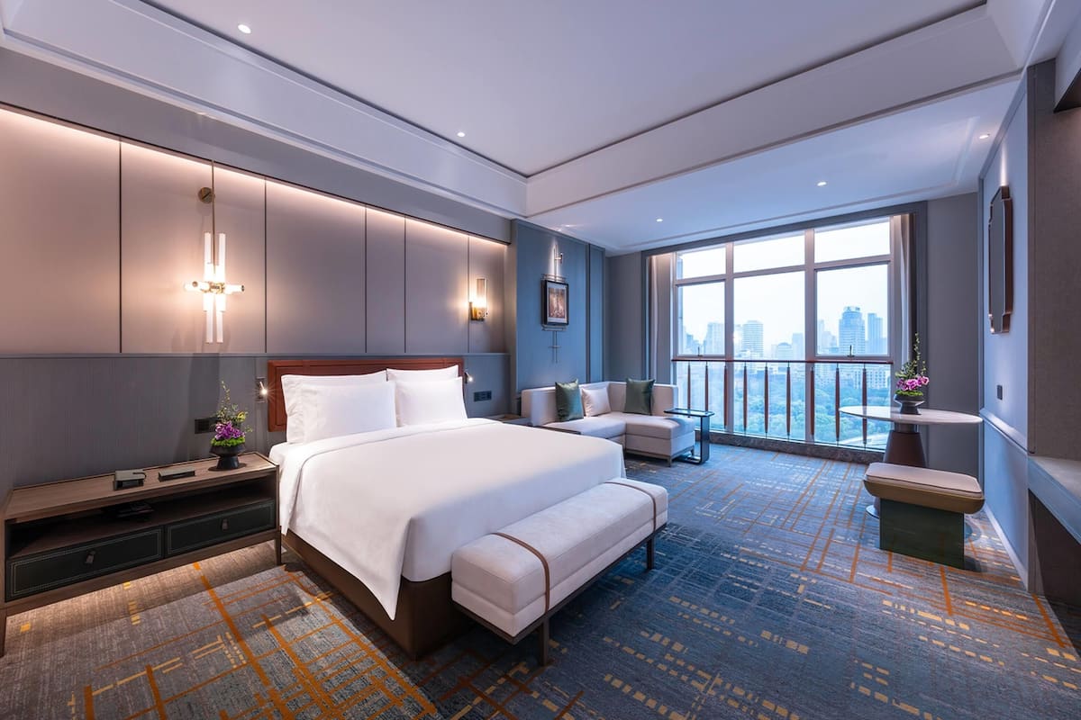 A modern hotel room with a large bed, a seating area, and a view of the city skyline.