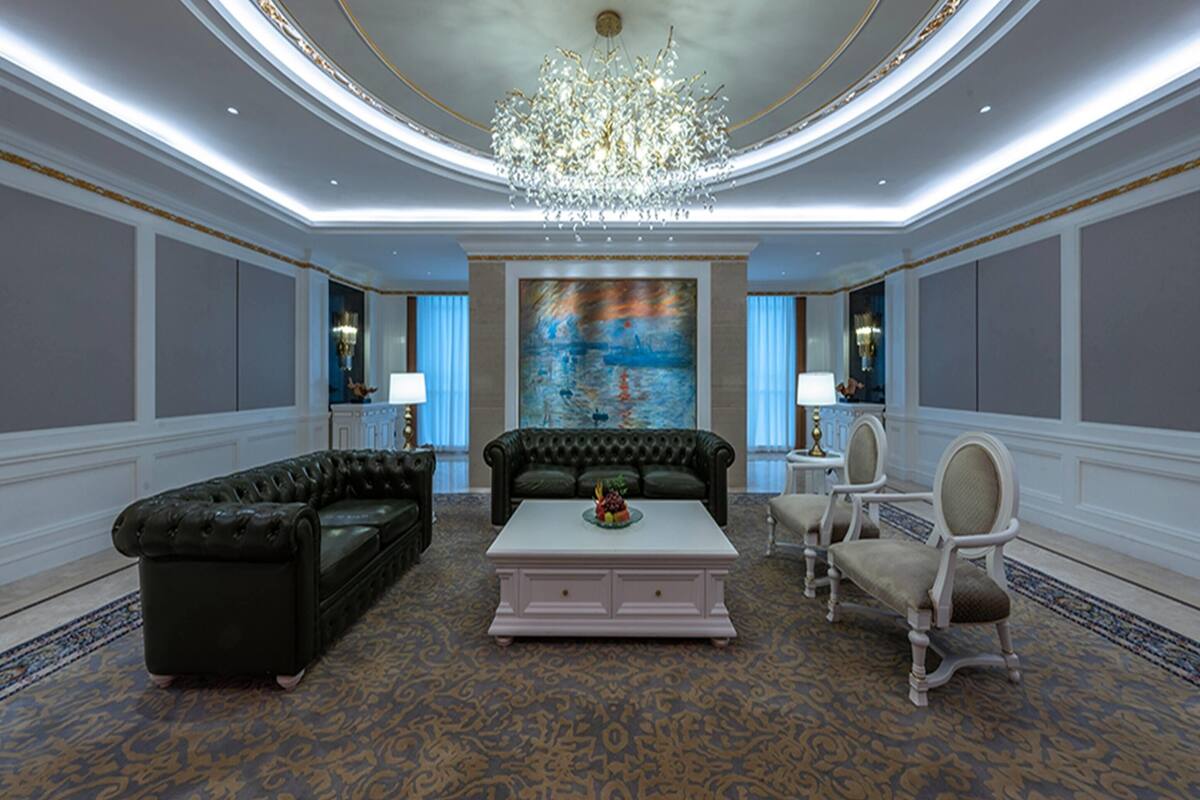A luxurious room with a chandelier, a large painting, a sofa, a coffee table, and two armchairs.