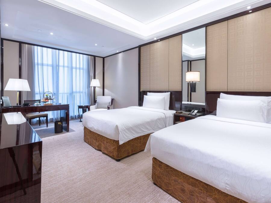 A hotel room with two beds, a desk, a chair, and a large mirror.