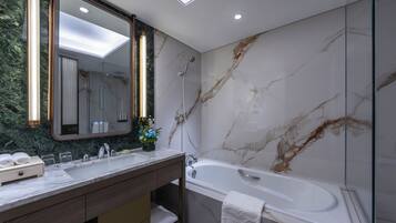 A modern bathroom with a marble wall, a large mirror, a bathtub, and a vanity with a towel rack.