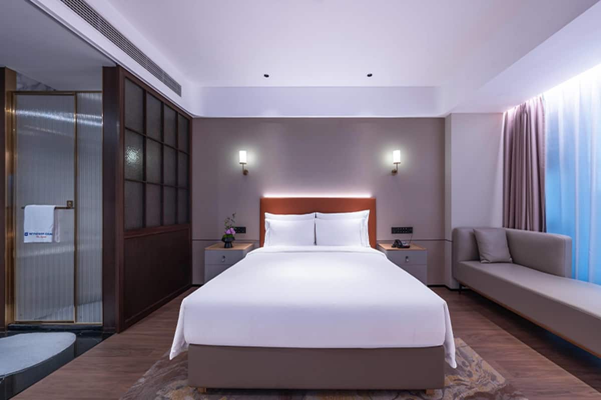 A modern hotel room with a large bed, bedside tables, a sofa, and a view of the city.