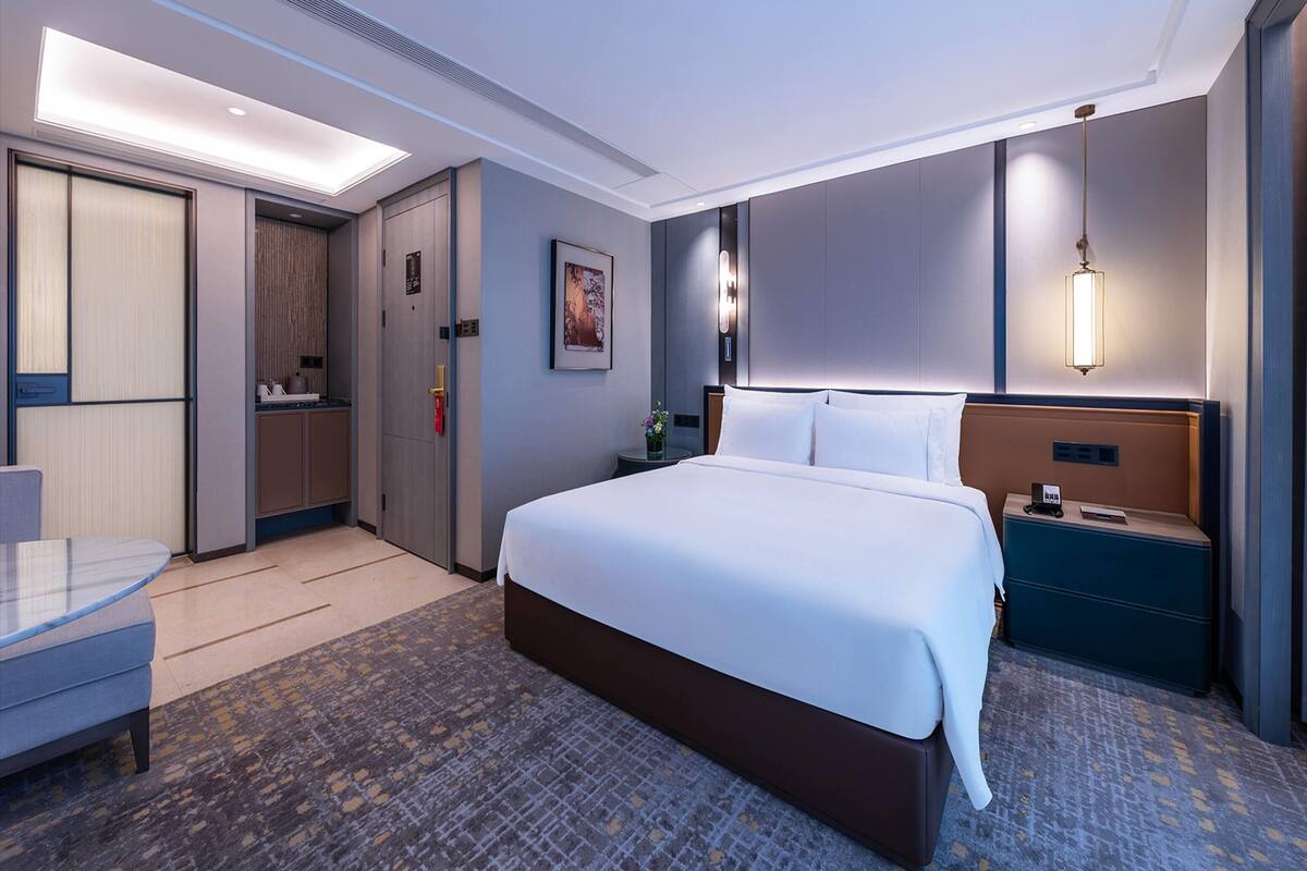 A hotel room with a large bed, bedside tables, a desk, and a wardrobe.