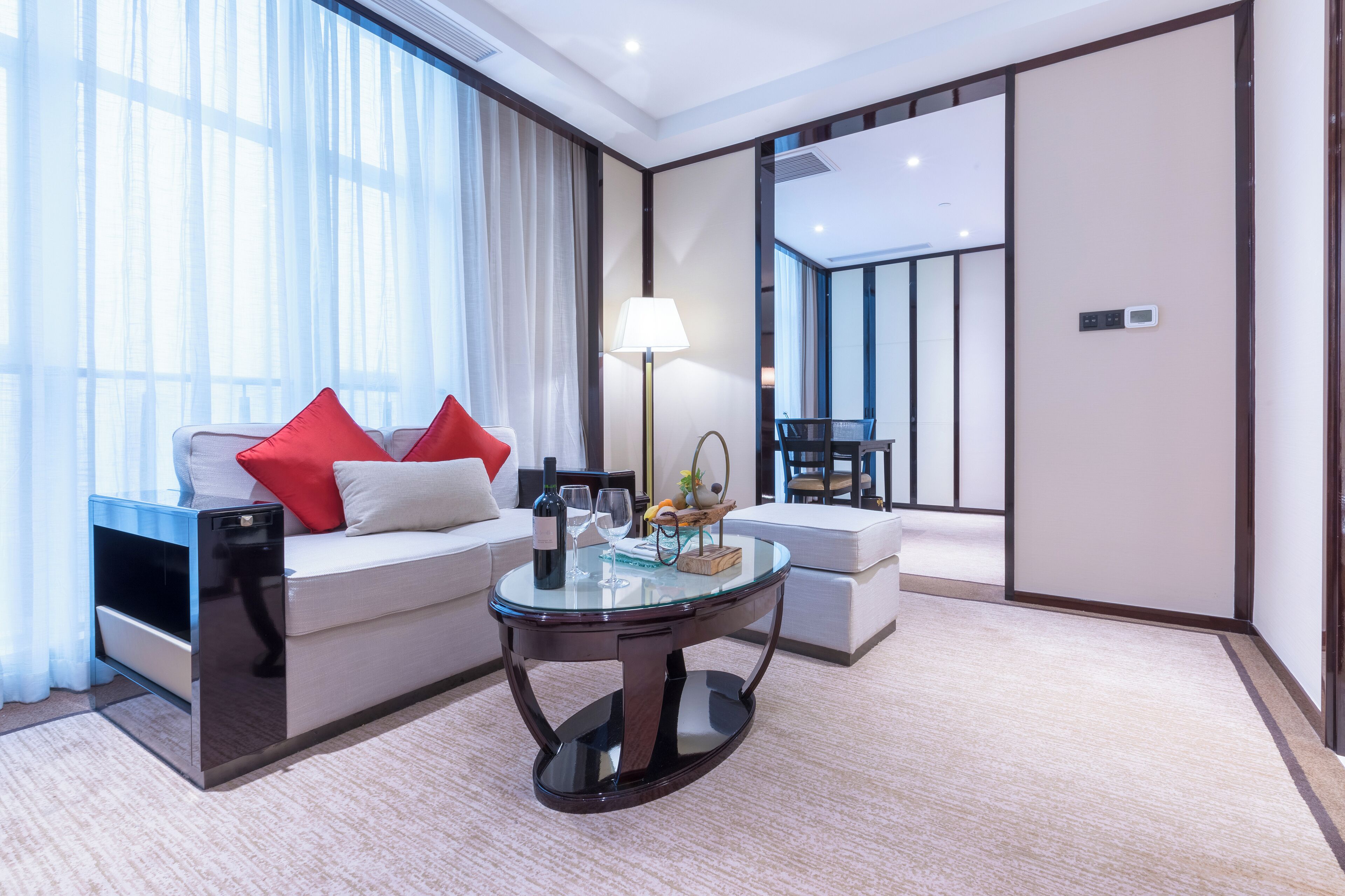 A modern hotel room with a sofa, a round glass table, a lamp, and a view of a balcony.