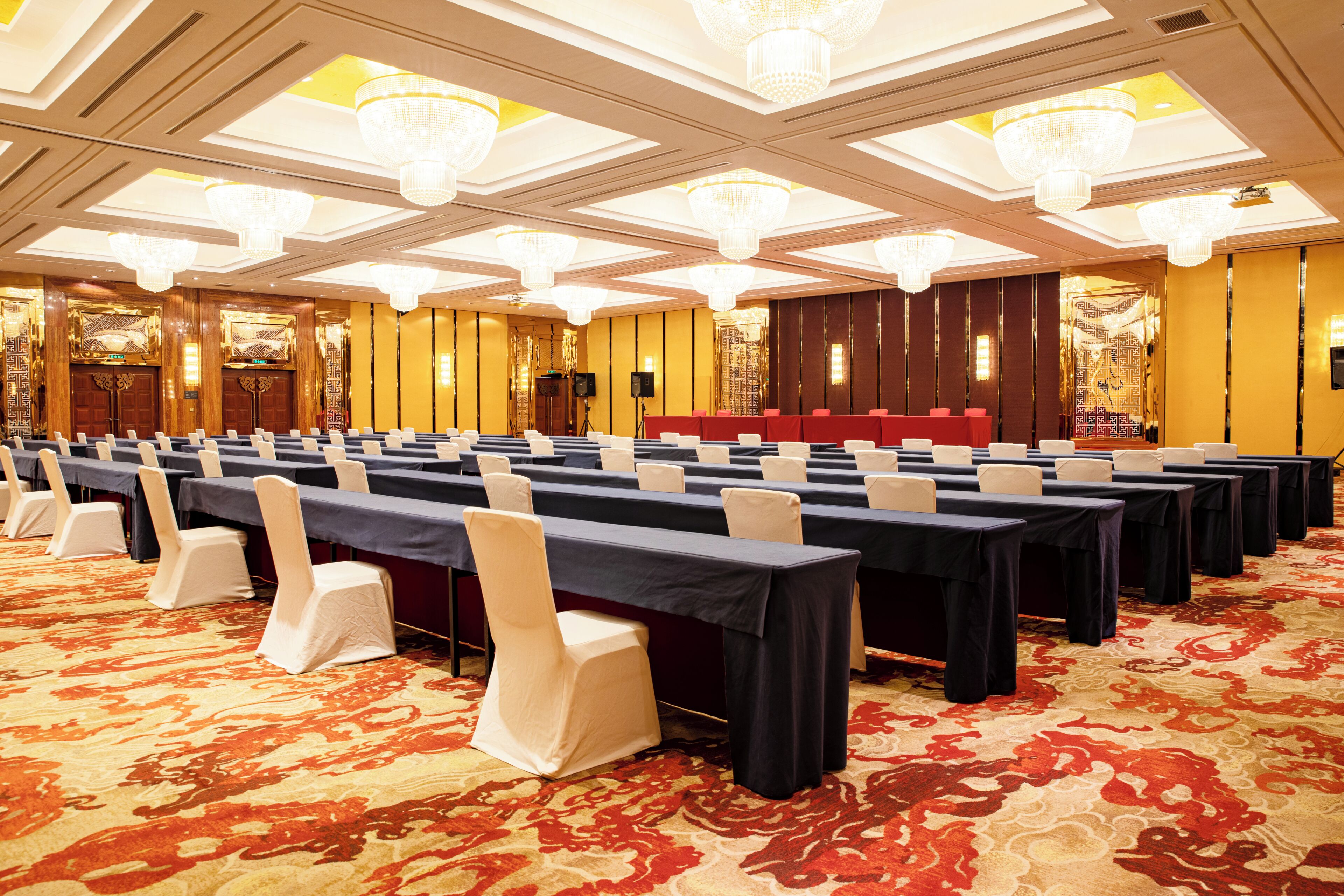 Un salón de conferencias con mesas y sillas dispuestas en filas, candelabros y un escenario.
