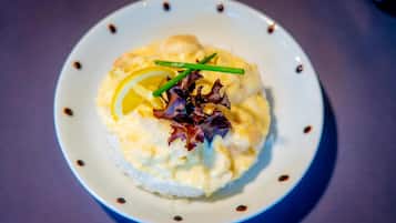Un plato de comida con una base cremosa, coronado con una rodaja de limón y cebollín verde, y adornado con una hoja de lechuga morada.
