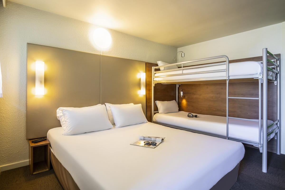 Ein Hotelzimmer mit einem Etagenbett, einem Nachttisch mit Fernbedienung und einer Zeitschrift auf dem Bett.