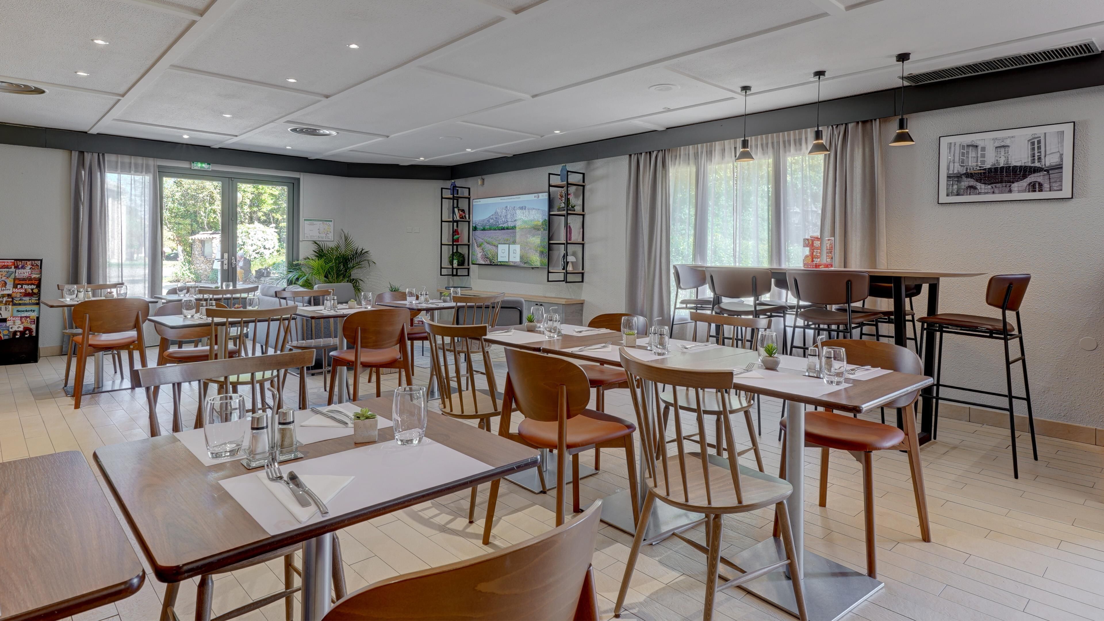 A restaurant with multiple tables and chairs, a large window with a view, and a ceiling with recessed lighting.